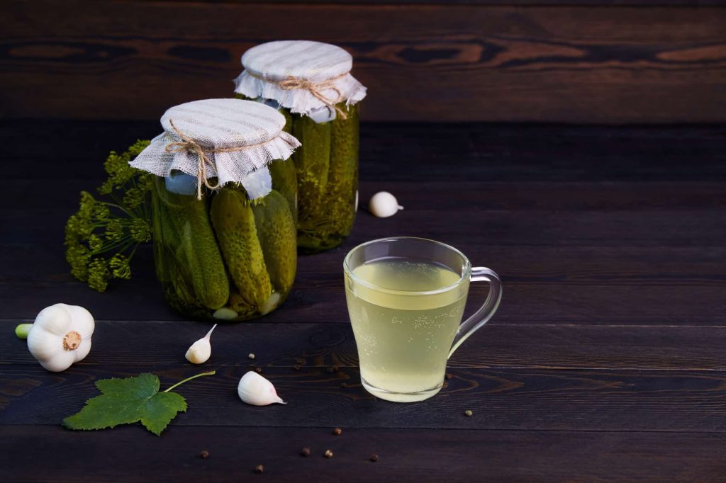 Pickled cucumbers in a jars, pickle juice in glass mug