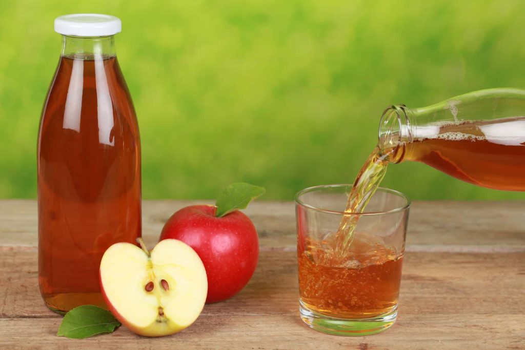 Fresh apple juice is pouring from a bottle into a glass