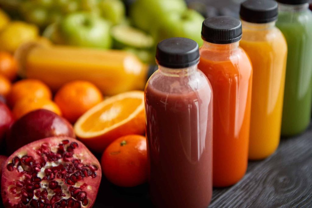 Bottles of fresh fruit juice in several colours on a black wooden table.