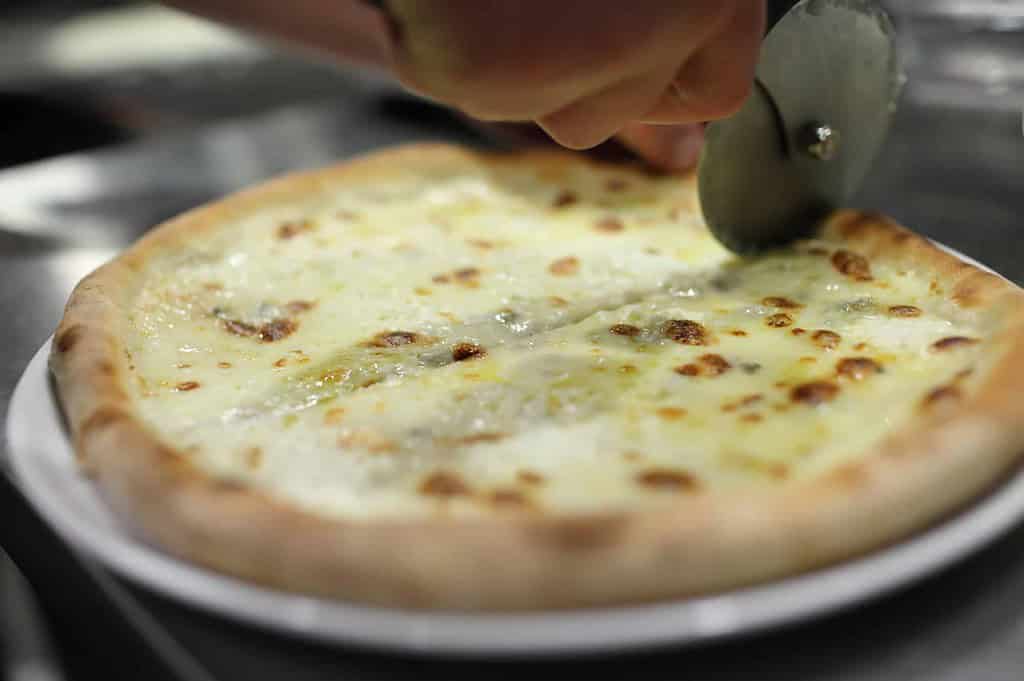 slicing white pizza using a pizza cutter